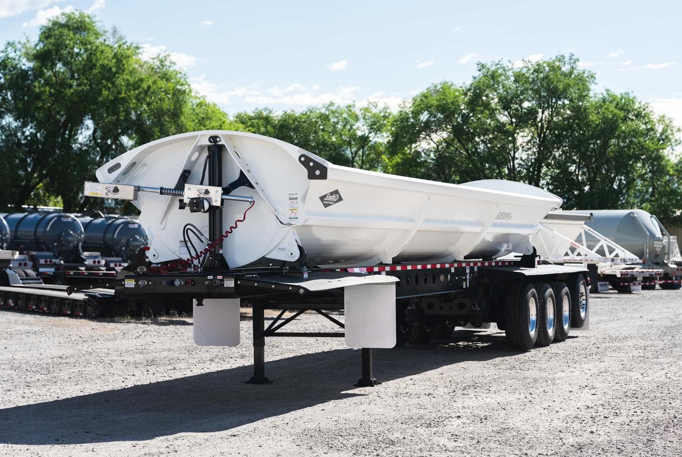 White SmithCo four-axle side-dump trailer photographed in an equipment yard